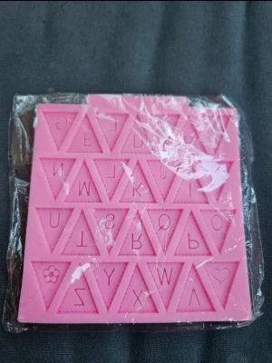 Silikonmatta bak - En rosa fyrkantig silikonform med alfabetet och siffror i triangulära fält. Perfekt för bakning, pyssel eller DIY-projekt där du vill skapa bokstäver i choklad, sockerpasta eller liknande material.