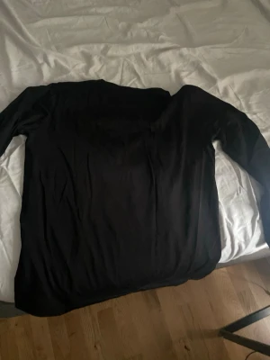 Svart stickad tröja - En enkel svart stickad tröja med lång ärm och rund hals. Tröjan har en klassisk passform och är tillverkad i ett mjukt material som passar perfekt till olika outfits. Perfekt basplagg för garderoben.