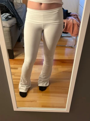 Vita utsvängda yoga pants  - Säljer ett par vita leggings med medel midja och utsvängda ben. De är stretchiga och sitter tight över låren men släpper ut vid anklarna. Perfekta för en avslappnad och trendig look. Materialet känns mjukt och bekvämt.