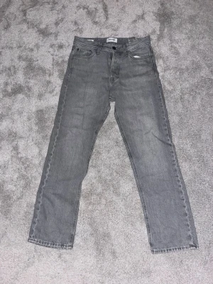 Jack and Jones jeans - Säljer ett par grå jeans med rak passform. Jeansen har normal midja och stängs med knapp. Materialet är denim i 100% bomull och färgen är en snygg tvättad grå nyans. Knappt använda stolek 27 30