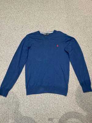 Mörkblå Ralph lauren tröja  - Klassisk mörkblå tröja med rund halsringning och diskret röd logga broderad på bröstet. Tröjan har långa ärmar och ribbade muddar vid ärmslut och nederkant. Perfekt till jeans eller chinos för en stilren look.