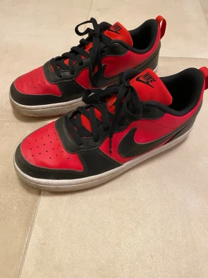 Nike sneakers - Hej! Säljer snygga Nike sneakers i rött och svart med klassisk swoosh-logga på sidorna. Skorna har lågt skaft, svarta snören och perforerad tå för extra ventilation. De är i storlek 40 och i riktigt bra skick. Perfekta för sommaren och till skolan! Tveka inte att höra av dig vid frågor!