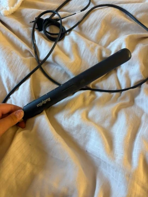 Svart plattång från BaByliss - Säljer en svart plattång från BaByliss med sladd. Plattången har en smal och avlång form, perfekt för att styla håret. Tillverkad i plast och metall med en enkel on/off-knapp på sidan.