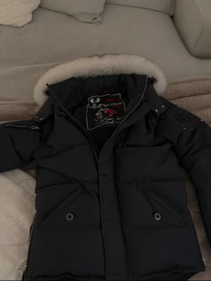 Svart dunjacka Moose Knuckles - Moose Knuckles 3Q Jacket herr i storlek M. Modell MK2228M3Q. Oanvänd och i mycket fint skick. En varm och stilren vinterjacka av hög kvalitet.  Märke: Moose Knuckles Modell: 3Q Jacket / MK2228M3Q Storlek: M Skick: Oanvänd