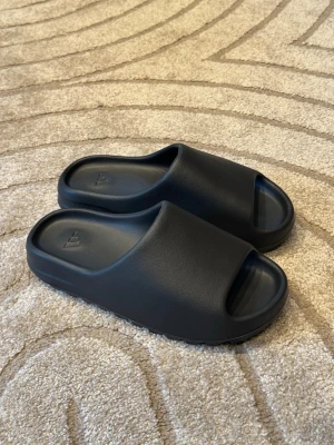 Adidas Yeezy slides  - Säljer ett par mörkgråa Adidas yeezy slides  i nästintill nyskick. Extremt sköna och mjuka skor. 