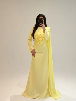 Lång gul klänning med drapering - Elegant lång klänning i ljusgul färg med draperad överdel och lång cape-detalj på ena axeln. Klänningen har långa ärmar och figurnära passform, perfekt för speciella tillfällen. Tillverkad i ett mjukt, flytande material som ger ett exklusivt intryck. Den är mer modest och skulle absolut säga hijabi vänlig , men funkar också för dig som gillar att sticka ut och ändå vara heltäckt. Aldrig använt klänningen innan då jag tyckte den var lite för liten. Originalpriset är 2200kr, säljer den för 1700kr.