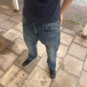 Levi’s 527 Bootcut - Säljer ett par blå bootcut jeans med snygga slitningar på låren och klassisk femficksdesign. Jeansen har normal midja och är tillverkade i denim med lätt stretch. Perfekta för en avslappnad och trendig look.