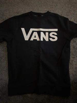 Svart Vans t-shirt med stor logga - Svart t-shirt från Vans med stor vit logga över bröstet. Klassisk rund halsringning och korta ärmar. Perfekt för en avslappnad streetwear-look.