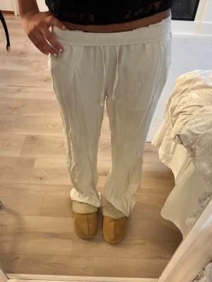 Vita linnebyxor med dragsko - Säljer ett par vita linnebyxor med avslappnad passform och resår i midjan samt dragsko för justerbarhet. Byxorna har raka ben och sidofickor. Perfekta för en chill och luftig stil under varma dagar.