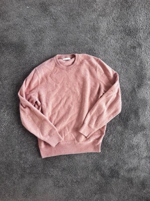 Rosa stickad tröja med rund hals - Mysig rosa stickad tröja med rund halsringning och långa ärmar. Tröjan har ribbade muddar vid ärmslut och nederkant, vilket ger en klassisk och enkel look. Perfekt för lager på lager under kyliga dagar. Tröjan är egentligen storlek M men har krympt och passar då väldigt litet (xs/ s)