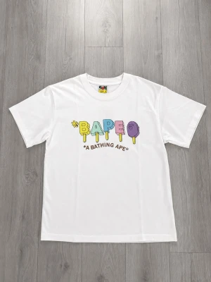 Vit Bape T-Shirt Storlek S - Det här är en Bape Tee ifrån säsongen summer/spring 2023, den är helt ny och har aldrig använts. Den kommer med alla tags som följer med vid köp. Den är perfekt för streetwear, vardags tröja eller så kan man ha den vid speciella tilfällen. Det är storlek S och den är True To Size. Tvättinstruktionerna sitter i taggen (se sista bilden)