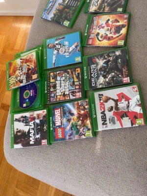 50  per st Xbox One spelpaket med 11 titlar - Säljer ett paket med 11 Xbox One-spel, bland annat GTA V, FIFA 19, Gears of War 4, Mafia III, NBA 2K19, LEGO Marvel Super Heroes 2, The Incredibles och Dragon Ball FighterZ. Alla spel i gröna plastfodral med färgglada omslag. Perfekt för dig som gillar action, sport och äventyr.