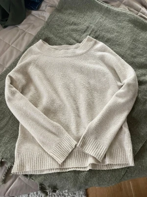 Vit/kräm färgad stickad tröja från Vero Moda - Mysig vit stickad tröja från Vero Moda med rund halsringning och ribbade muddar vid ärmslut och nederkant. Tröjan har en avslappnad passform och är perfekt för lager på lager. Materialet känns mjukt och bekvämt mot huden. Tröjan är nopprig. 