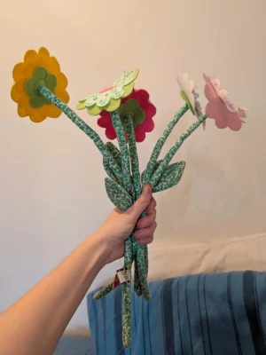 Tygblommor i olika färger - Säljer ett gäng tygblommor i glada färger som gul, rosa, grön och röd. Blommorna har mjuka stjälkar och blad i grönt tyg med mönster. Perfekt som dekoration till rummet eller som present till någon du gillar.