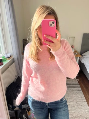 Ljusrosa stickad tröja Selected Femme i Ull och Alpacka - Mysig ljusrosa stickad tröja från Selected Femme. Tröjan har rund halsringning, långa ärmar och är gjord i ett fluffigt, mjukt material som känns lyxigt. I ull och alpacka. Perfekt för att hålla värmen under kyliga dagar och enkel att styla med jeans eller kjol.