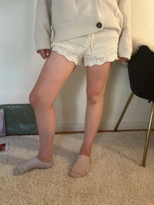 Vita virkade shorts med volangkant - Säljer ett par vita virkade shorts med snygg volangkant och detaljerat mönster. Shortsen har en hög midja och är perfekta för sommarens alla tillfällen. De är gjorda i mjuk bomull och har en avslappnad passform.
