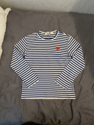 Comme des Garçons tröja (Randig) - Säljer en skitsnygg  randig långärmad CDG-tröja med det röda hjärtat. Den är helt oanvänd/nyskick (bara provad). Obs: Tvättlappen på insidan är bortklippt för den skavde, men nacklappen sitter kvar! Skriv om du undrar över något eller vill ha fler bilder! Kan skickas eller mötas upp. 
