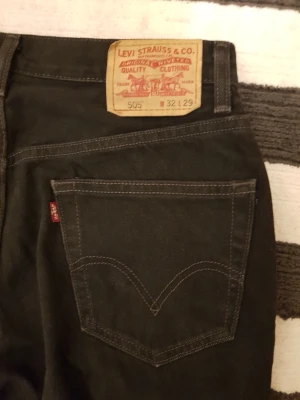 Svarta Levi's 505 jeans - Säljer ett par svarta Levi's 505 jeans med raka ben och klassisk femficksdesign. Jeansen har slitningar framtill för en cool, avslappnad look och är tillverkade i bomull. Perfekta för dig som gillar streetstyle och tidlös denim.