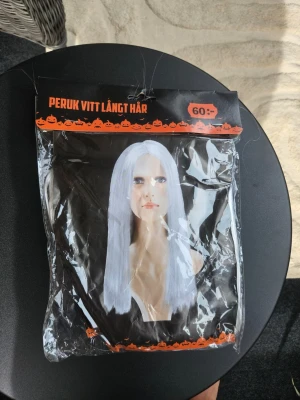 Vit lång peruk till maskerad - Säljer en vit lång peruk perfekt för maskerad eller cosplay. Peruken har rakt hår och en mittbena, och är tillverkad i syntetmaterial. Passar till halloween, temafester eller när du vill ha en cool look.