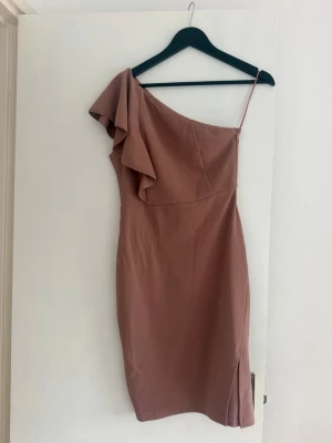 Rosa one shoulder klänning Bubbleroom - Säljer en snygg rosa one shoulder klänning från Bubbleroom i storlek 36. Klänningen har volangdetalj vid axeln, smal passform och slits nertill. Perfekt för dig som vill sticka ut med en unik och trendig look.