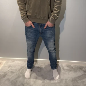 Nudie jeans - Snygga blå Nudie jeans med slim passform och klassisk femficksdesign. Jeansen har en lätt tvättad look, bruna detaljer på bakfickorna och smal siluett som sitter tajt vid benen. Perfekta för dig som gillar stilrena och moderna jeans. Modellen är 186cm och väger 70kg