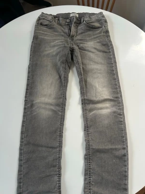 Grå slim fit jeans - Snygga grå slim fit jeans med klassisk femficksdesign och lätt slitna detaljer på framsidan. Jeansen har normal midja och raka ben. Perfekta till en avslappnad streetstyle-look. Materialet är mjukt och stretchigt för extra komfort.