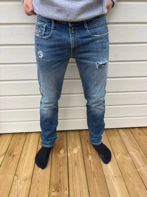 Blå Replay Anbass slim fit jeans - Säljer ett par blå Replay Anbass jeans i slim fit-modell. Jeansen har klassisk femficksdesign, snygga slitningar och detaljer på bakfickan. Tillverkade i denim med en skön passform och modern look.
