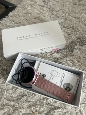 Smartklocka med rosa mesh-armband - Snygg smartklocka med rund urtavla och rosa mesh-armband i metall. Kommer i originalförpackning med laddkabel och manual. Perfekt för dig som vill ha koll på notiser och hälsa direkt på handleden. Aldrig använd 