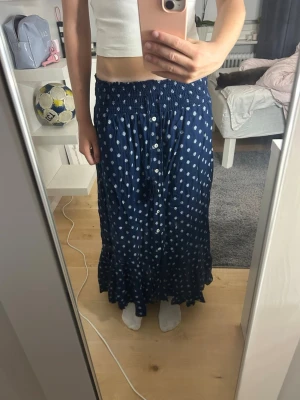 Marinblå långkjol med vita detaljer  - Säljer en marinblå långkjol med vita detaljer och knappar framtill, säljer då den inte används så mycket💕