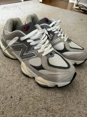 New balance 9060 - Stilrena sneakers från New Balance i grått och vitt med inslag av svart. Skorna har en chunky sula, meshpaneler för ventilation och mockadetaljer. Klassisk N-logga på sidan och vita skosnören. Perfekta för en sportig och trendig look.