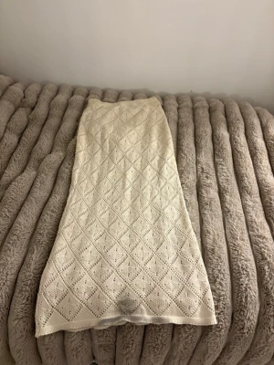Beige stickad långkjol med hålmönster - Säljer en beige stickad långkjol med ett detaljerat hålmönster i diamantform. Kjolen har en rak passform och är perfekt för dig som gillar en bohemisk och avslappnad stil. Superfin att matcha med en enkel topp eller stickad tröja.