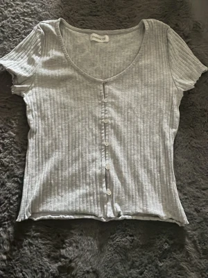 Ljusgrå topp med knappar - Säljer en ljusgrå topp från Even&Odd med korta ärmar och knappar framtill. Toppen har en rundad halsringning och är i ett mjukt, stretchigt material. Det står ingen storlek i den, men jag skulle nog säga att den är S. Pris kan diskuteras och skriv gärna om funderingar 💞💞