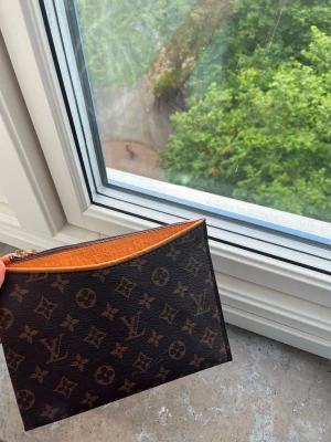  kuvertväska - Snygg kuvertväska  i klassiskt brunt monogrammönster med guldiga detaljer och dragkedja. Väskan har en slimmad, rektangulär form och insidan är fodrad i ljust läder. Perfekt för att bära det viktigaste med stil.