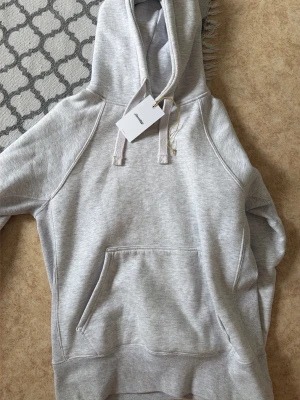 Ljusgrå hoodie med huva och magficka - Snygg ljusgrå hoodie med klassisk huva och dragsnören. Hoodien har en stor magficka framtill och ribbade muddar vid ärmslut och nederkant. Tillverkad i mjukt sweatshirtmaterial som är perfekt för chill dagar.