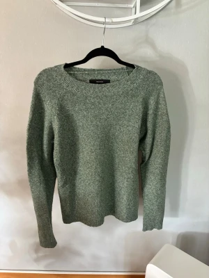 Grön stickad tröja med rund hals - Mysig stickad tröja i melerad grön färg med rund halsringning och långa ärmar. Tröjan har ribbstickade muddar vid ärmslut och nederkant. Perfekt för kyliga dagar och enkel att matcha med olika outfits.