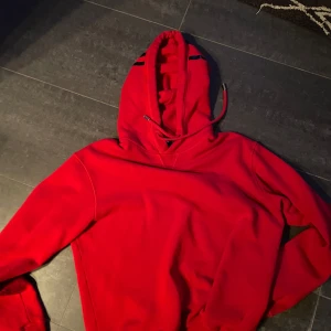 Röd hoodie från DSQUARED2 - Säljer en röd hoodie från ICON med svart tryck på huvan och dragsko. Tröjan är i använt skick . Storlek M, Köpt på NK i stockholm, säljer för 400 kr
