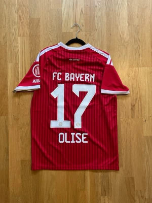 Olise #17 - M - Säljer en röd FC Bayern München matchtröja från Adidas med vita detaljer och nummer 17 Olise på ryggen. Tröjan har klubbmärke och sponsorloggor på bröstet samt korta ärmar med vita ränder på axlarna. Perfekt för fotbollsfans!
