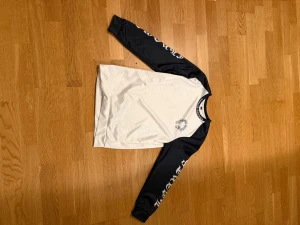Vit och svart långärmad T-shirt  - Säljer en vit och svart långärmad t-shirt med tryck på ärmarna och runt halsen. Tröjan har kontrastfärgade ärmar och rund halsringningen. Perfekt för dig som gillar streetwear vibes.