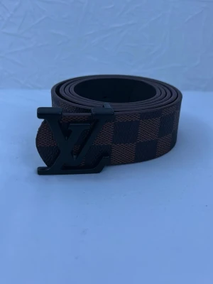 Bälte  - Snyggt bälte med klassiskt rutigt mönster i brunt och mörkbrunt design. Bältet är gjort i skinn och har en stilren look som passar till många outfits. Storlek 120 och är i helt ny skick . Pris kan diskuteras!