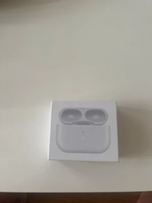 Airpods laddningsfodral  - Säljer ett par vita trådlösa in-ear hörlurar med laddningsetui. Snygg och kompakt design i plast, perfekt för dig som vill ha smidiga hörlurar till mobilen. Laddningsetuiet är stilrent och lätt att ta med sig överallt.