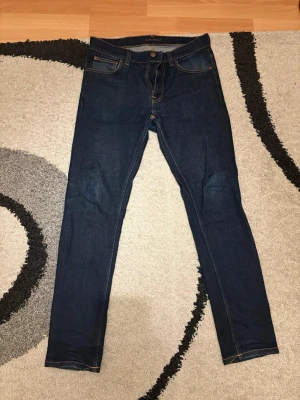Nudie jeans Lean Dean  - Snygga mörkblå slim fit jeans med klassisk femficksdesign och kontrastsömmar. Jeansen har en rak midja och smala ben, perfekta för en clean och stilren look. Tillverkade i stretchigt denimtyg för extra komfort.