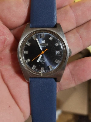 Tissot vintage klocka blått band - Säljer en klassisk Tissot vintageklocka med svart urtavla, datumvisning och orange sekundvisare. Boetten är i silverfärgad metall och armbandet är blått med beige undersida. Perfekt för dig som gillar retrostil och schweizisk design. Behövs batteri , säljs i befintligt skick. Skakar man på klockan tickar den igång ett par sek 