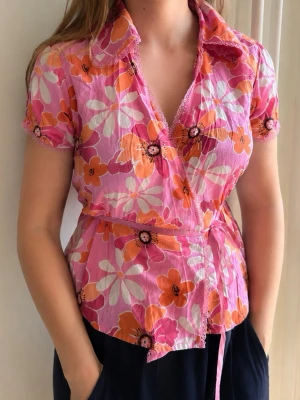 Vintage rosa blommig topp - Vintage sommartopp i rosa med spetsdetaljer och blommigt mönster. Storlekslapp saknas, men passar uppskattningsvis storlek S/M. I perfekt skick och kommer med originaletiketter. Ett vackert archive-plagg.