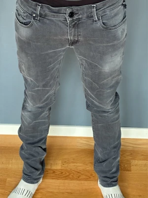 Grå slitna slim fit jeans - Snygga grå jeans i slim fit-modell med slitna detaljer och tvättad look. Klassisk femficksdesign och knappgylf. Jeansen har en modern passform som sitter tajt över benen  och passar perfekt till en avslappnad stil. Modellen är 176 lång o väger 61 kg 