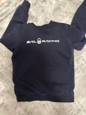 PRIS KAN DISKUTERAS!Mörkblå Sail Racing sweatshirt - Mörkblå sweatshirt från Sail Racing med vit logga tryckt över bröstet. Klassisk rund halsringning och ribbade muddar vid ärmslut och nederkant. Mjuk insida och stilren design som passar perfekt till jeans eller joggers.PRIS KAN DISKUTERAS!