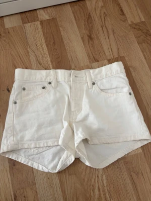 Vita denimskorts med broderade fickor - Snygga vita skorts i denim med klassisk femficksdesign och broderade detaljer på bakfickorna. Hög midja och bälteshällor för extra stilpoäng. Perfekta för en fräsch och trendig look i sommar.