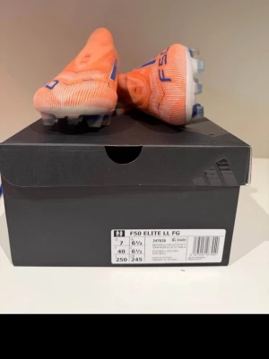 Adidas F50 Elite LL FG orange - Säljer ett par Adidas F50 Elite LL FG fotbollsskor i orange med blå detaljer och vita sulor. Skorna har låg vikt, strömlinjeformad design och är tillverkade i syntetmaterial för bästa prestanda på fasta underlag. Medföljer matchande orange påse.