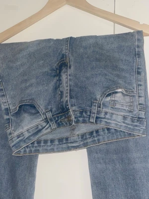 Blå utsvängda jeans med hög midja - Säljer ett par blå jeans med utsvängda ben och hög midja. Klassisk femficksmodell med knapp och dragkedja framtill. Jeansen har en snygg tvättad look och är tillverkade i denim. Perfekta för dig som gillar retrostil och vill ha ett par statement-jeans.