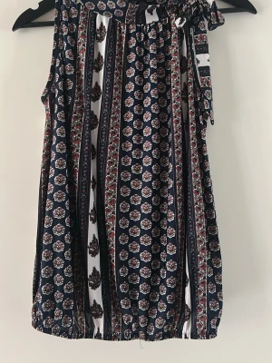 Mönstrad ärmlös topp - Snygg ärmlös topp med marinblå och vita ränder samt blommigt mönster i rött och vitt. Toppen har ett knyt vid axeln och är i en luftig modell, perfekt för varma dagar. Jag skulle säga att den passar som S/M