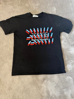 Maison Margiela T-shirt - Säljer nu en snygg och stilren svart tröja ifrån Maison Margiela, tröjan är köpt för ca 6 månader sedan. Andvänd ett fåtal gånger så skicket är som nytt! Pris är ej hugget i sten, hör av dig för fler bilder, eller allmän info :)